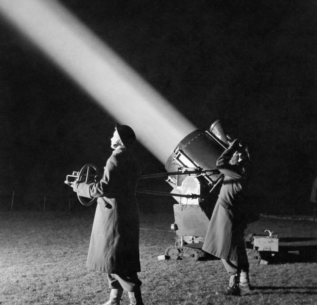 2 persons standing in front of a searchlight